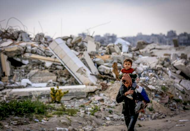 A boy carries a kid on his shoulders amid the rubble of the Jabalia Refugee Camp, Gaza.