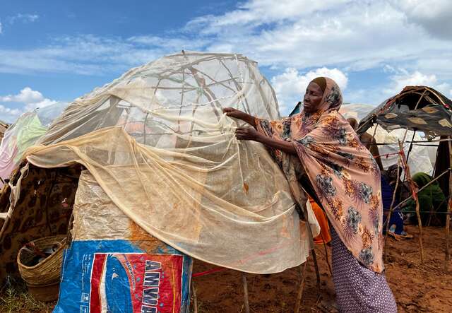 A woman works on improving her makeshift shelter in Somalia.