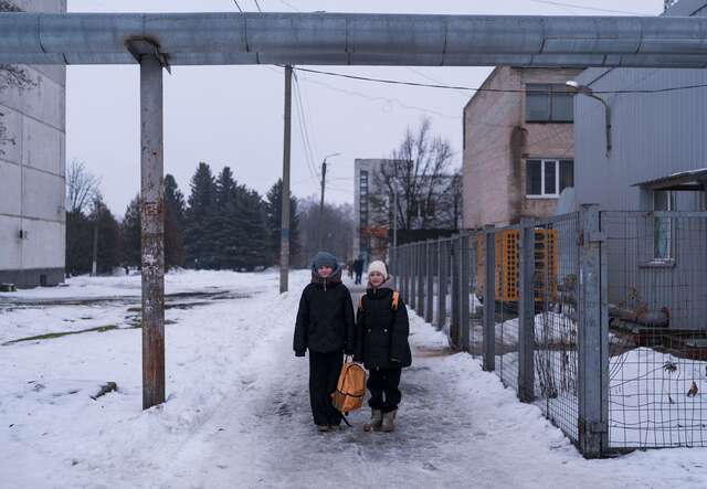 Two children walk down a snowy street in Ukraine.