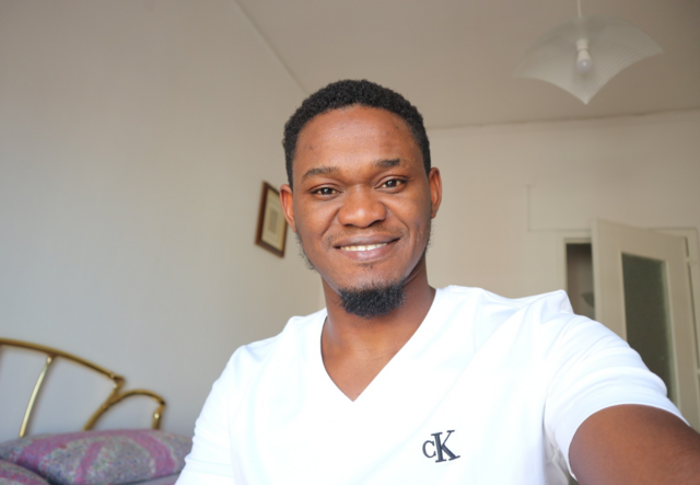 Henry Tbilisi, a refugee from Nigeria, wearing a white t-shirt smiling and looking at camera.