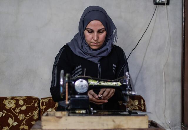 Um Abdo sits at her sewing machine making masks in Syria