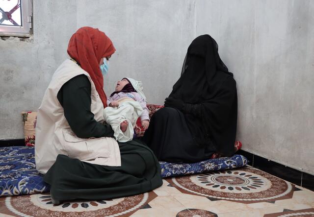 Bushra holding an infant and sitting next to a woman.