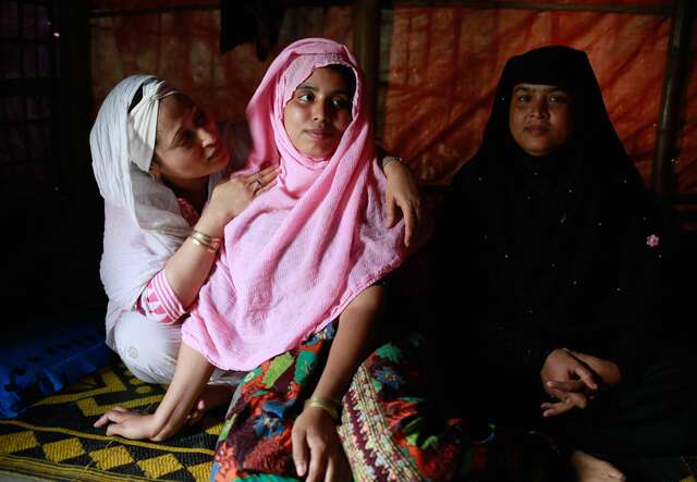 Razia Sultana visits a Rohingya family in Ukhiya camp. Three women sit together on the floor of a home.