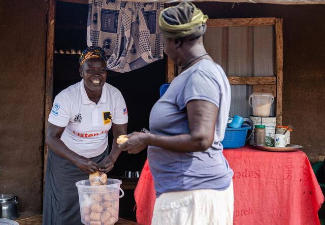 Jemimah Sadia talking to a woman while holding a bag of small cakes