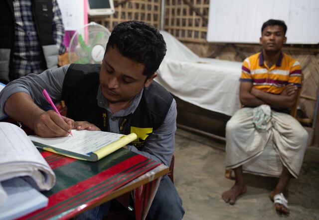 Dr Mahmudul Hossain writes out details of his patient who is sitting in the background with a bandaged foot.