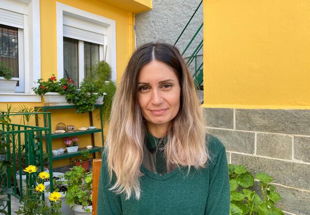 Kiki smiles at the camera outside a yellow house in Greece