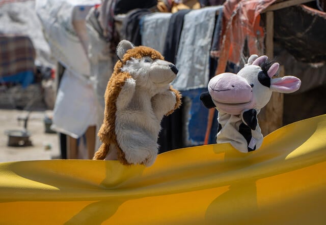 A fox and cow puppet interact with each other 