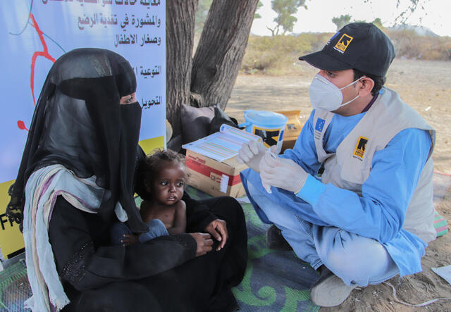 IRC staff member in Yemen talking to a client who holds her young daughter