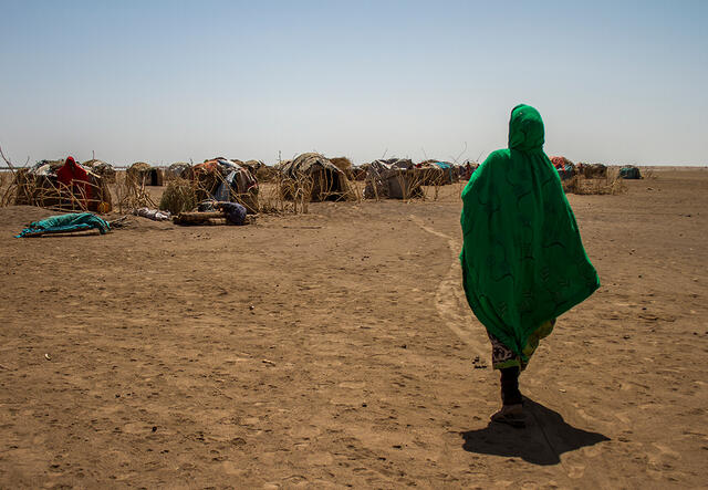 woman in green walks towards her temporary accommodation in Ethiopia desert.