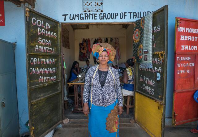 Domitila Kaliya standing in front of her sewing business in Kampala, Uganda
