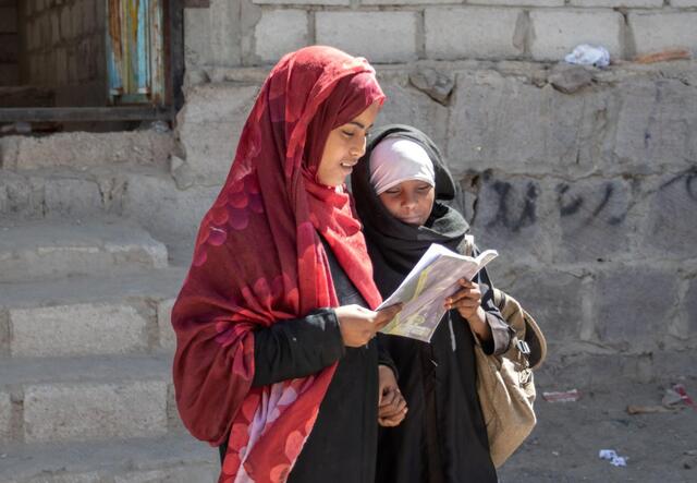 Aisha and Na’aem reading a book together on their way home from school. 