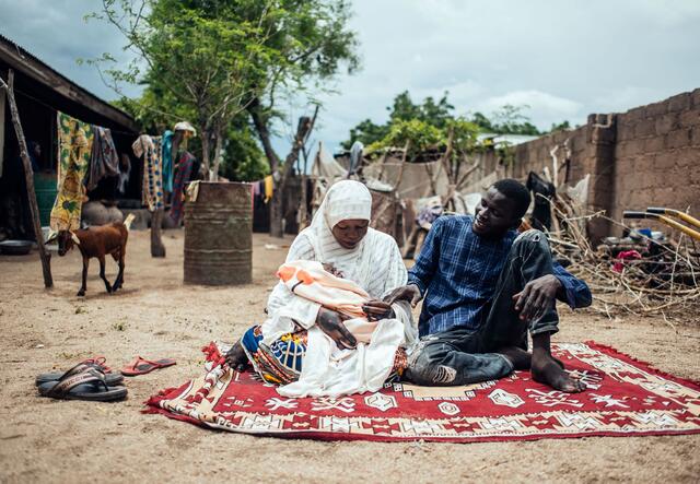 A young couple, Hussaini and Ibrahim, sitting on the ground on a rug with their newborn baby