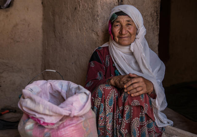 A woman in Afghanistan sits next to a bag of rice.