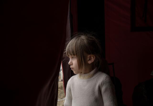 A young girl who had to flee Ukraine for Poland looking out of a tent