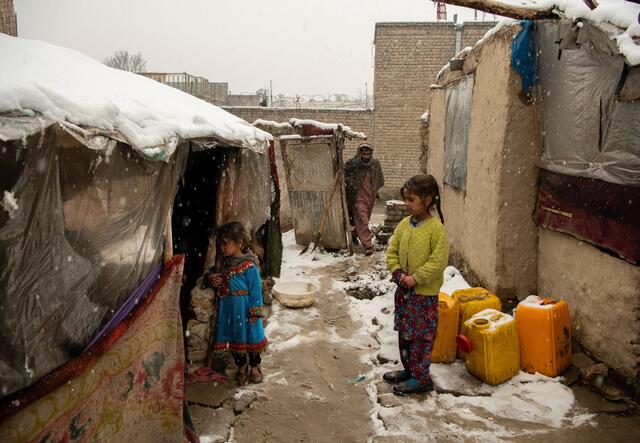 A man and two children standing outside a makeshift home in Kabul, Afghanistan.