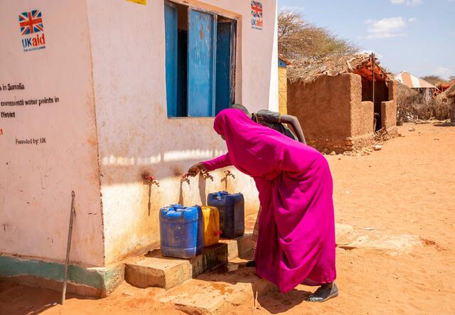 A woman, Fadumo, turns on a tap to fill a water can.