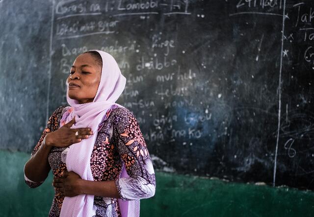 Standing by the blackboard, International Rescue Committee teacher Fatima demonstrates deep breathing techniques to her students.