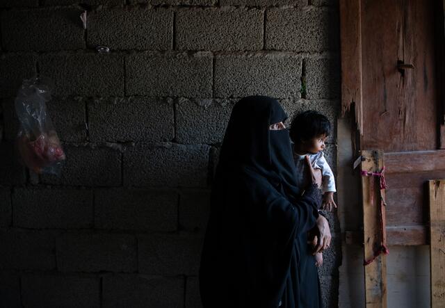 Adeeyah Aholds her toddler daughter Salaman in the dark kitchen of their temporary home in Yemen. The family received assistance from the International Rescue Committee.