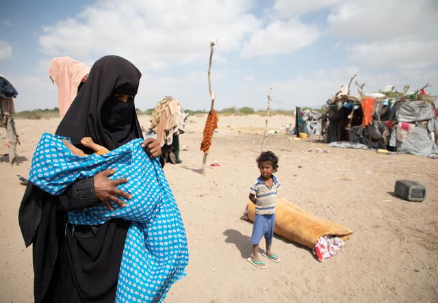 Nadia holds her baby son wrapped in a blanket outside her makeshift home in Yemen. The family received medical and nutrition assistance from the International Rescue Committee.