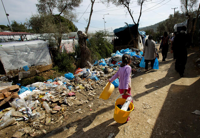 A young girl walks past tents and trash in an overcrowded refugee center