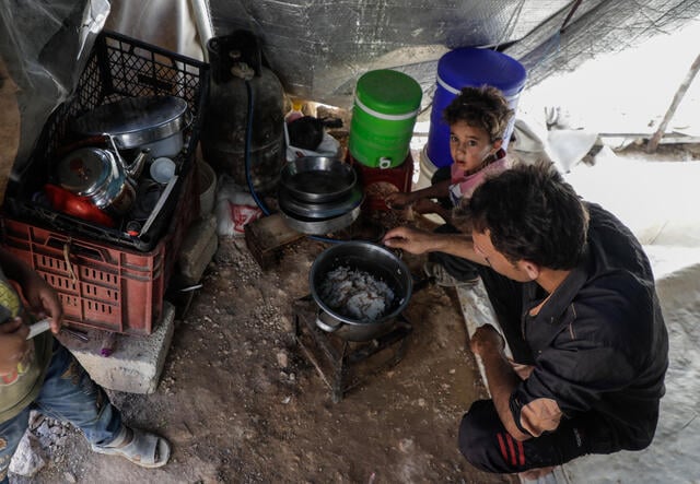 Naeem, 24, and his family around a cooking fire in their makeshift shalter in northern Idlib, where the IRC is assisting uprooted Syrians.