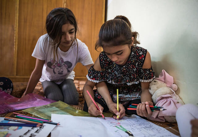 Two young sisters in Sinjar, Iraq sit on the floor coloring in an activity book  