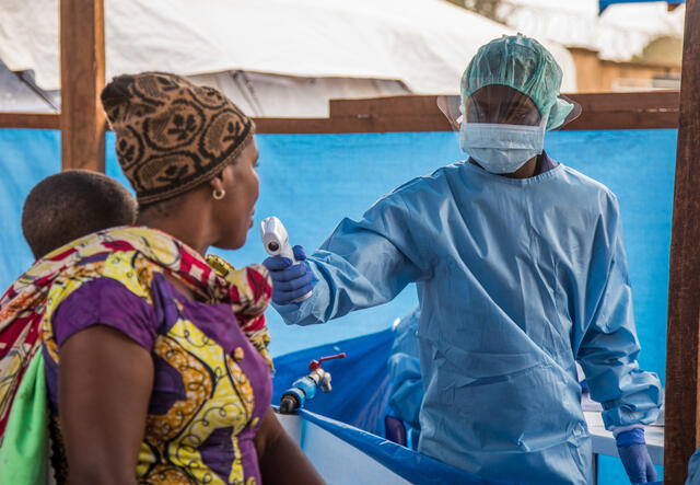 A health worker at Beni Hospital uses a scanning thermometer to check a woman carrying a baby for fever as they arrive at the hospital.