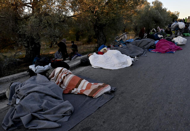 People wrapped in blankets sleep on a road after being displaced by a fire in Moria refugee camp in Lesbos, Greece.