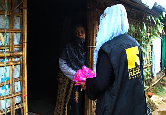 An IRC community volunteer greets a refugee from Myanmar at the door of her makeshift bamboo home in a Bangladesh refugee camp