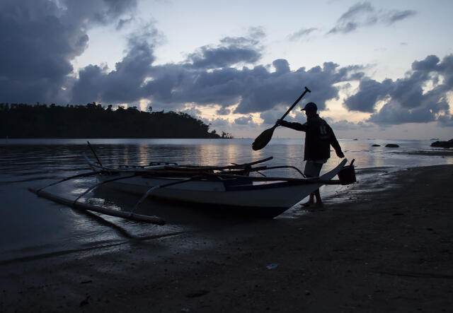 Fisherman gets into his boat as the sun rises on the beach