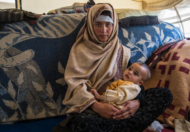 A displaced Afghan farmer sits holding her baby inside a tent.