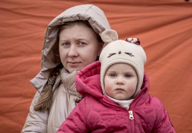 A Ukrainian mother wearing winter clothes holds her bundled-up baby at the Poland-Ukraine border after crossing.