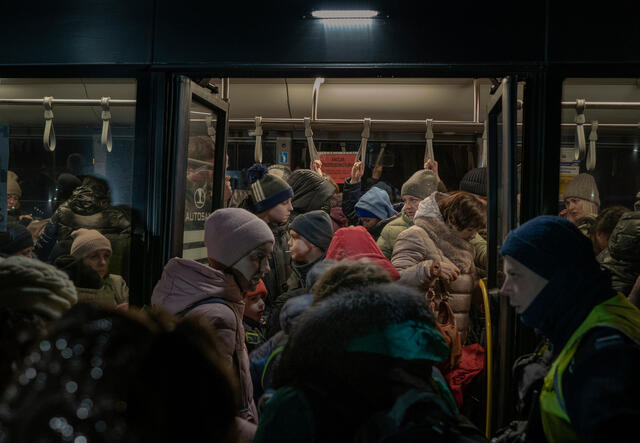 Refugees from Ukraine in winter coats wait to board a bus at the Ukraine-Poland border.