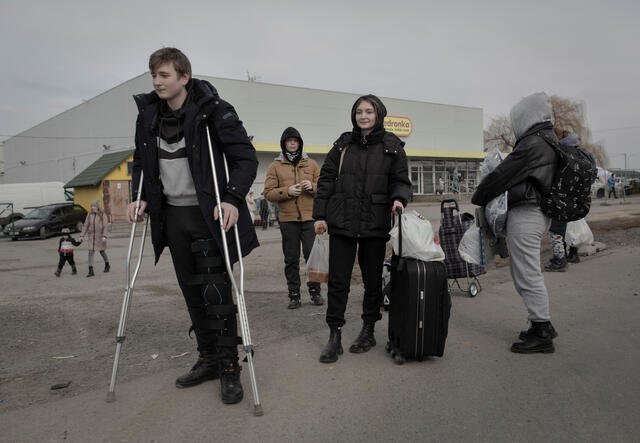A teenage boy from Ukraine using crutches waits in a line with family members carrying light lugage after fleeing across the border to Poland.