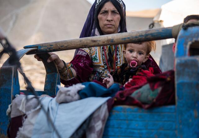 A mother rocks her sick child, who is sucking on a pacifier, in a camp in Afghanistan's Badghis province, where the IRC supports displaced families.
