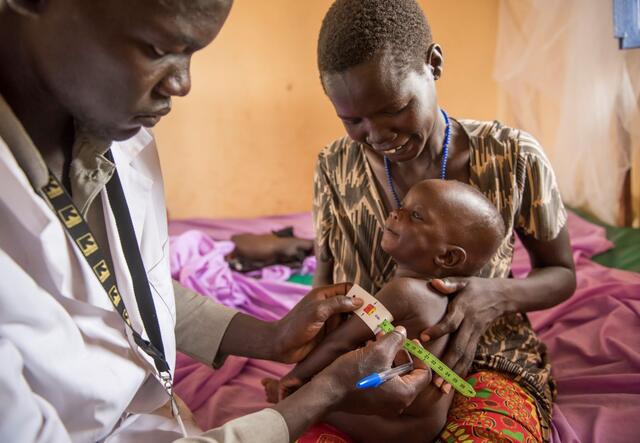 An IRC health worker examines a 7-month-old infant being held by his mother.