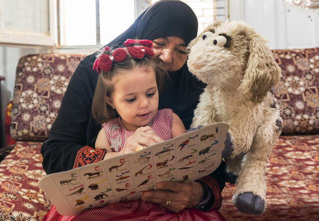 A child learns her letters and numbers alongside her caregiver and Ma’zooza, a new character from the Ahlan Simsim TV show.