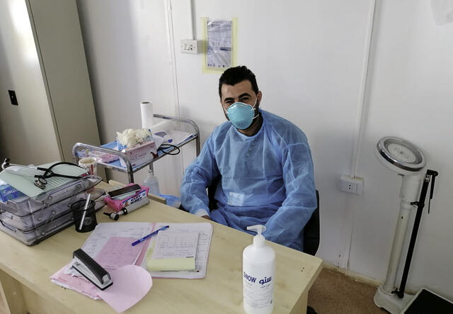 Dr Hazem sits behind his desk at the IRC's clinis. He is wearing a surgical mask and scrubs. 