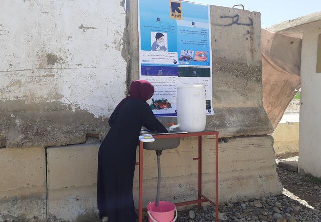 A woman washes her hands at an IRC handwashing station with an informational poster on a wall above her head. 