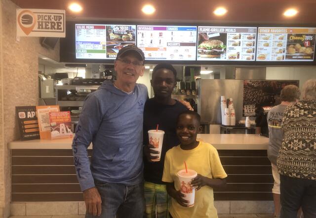 Tommy stand with his arm around Eric and Emmanuel in front of the Burger King counter. The boys hold large sodas and are smiling.