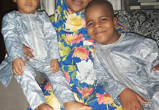 Dr Fatima Ibrahim Lawan poses with her children on either side of her as she sits on a couch.