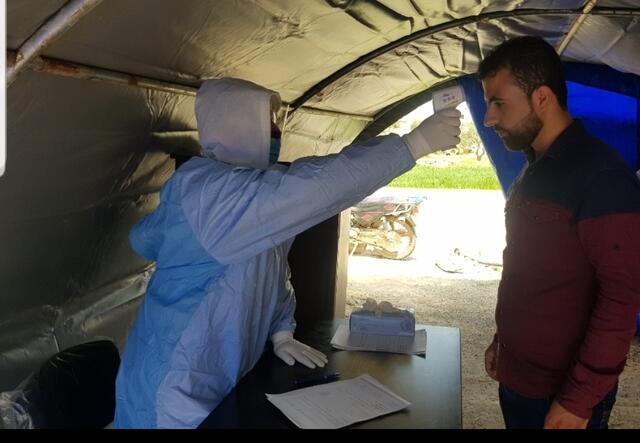 A health worker takes a patient’s temperature before they enter a clinic run by the IRC in a town in northwest Syria.