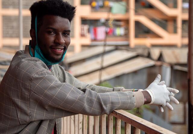 Jean Marie Ishimwe, a youth advocate and Rwandan refugee living in Kenya, leans against a railing with buildings behind him.