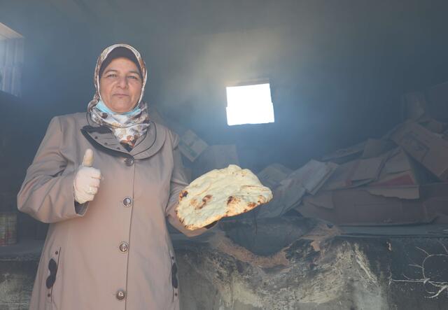 Mariam gives a thumbs up. She is wearing a grey coat. 