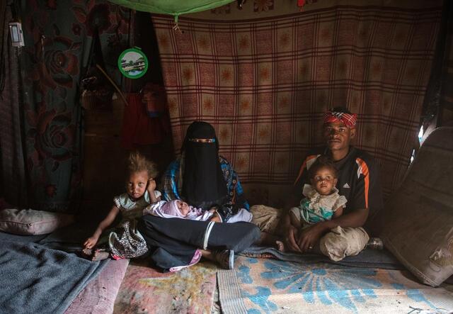 Bodor, 28, holding her baby daughter Enqath, sits with her husband and two children inside their tent. The baby is sitting on Bodor's lap and another child sits on her husband's lap. The whole family is looking at the camera.