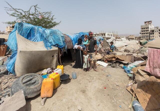 Bodor and her family stand together outside of the displacement camp where they live in the Al Dhale'e region in Yemen. They are standing in front of a makeshift tent.  