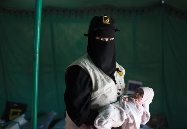 An IRC staff member, wearing an IRC vest, holds Enkath. 