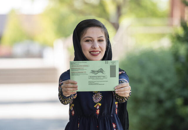 Muska Haseeb smiles and holds her mail-in ballot out to the camera 