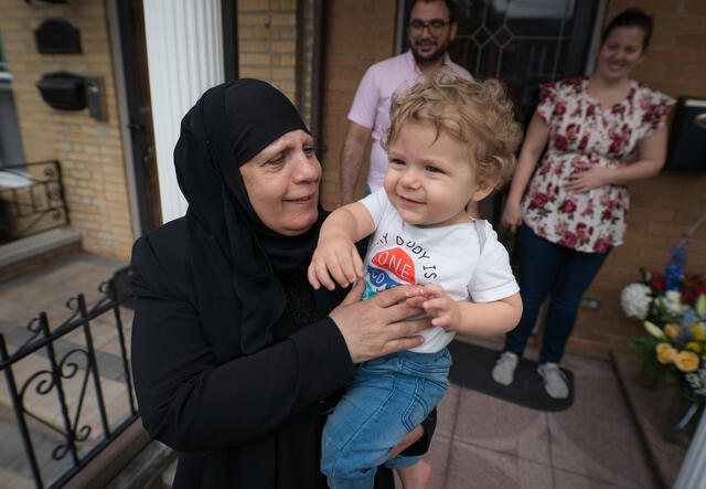 Maha holds her grandson and looks at him smiling. 