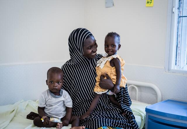 A mother sits on a hospital bed with her two young children in the Nigeria health center where they were being treated for acute malnutrition,